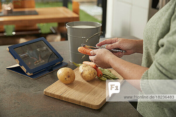 Woman with tablet PC peeling carrot preparing meal at home