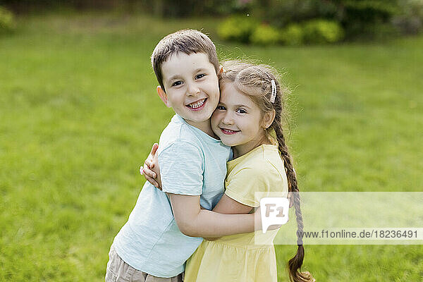 Smiling brother hugging sister standing in garden