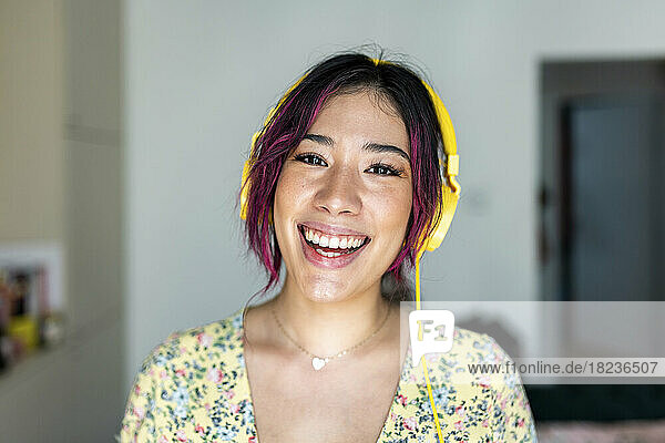 Happy young woman wearing headphones listening to music at home
