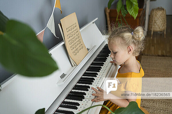 Blond girl practicing piano at home