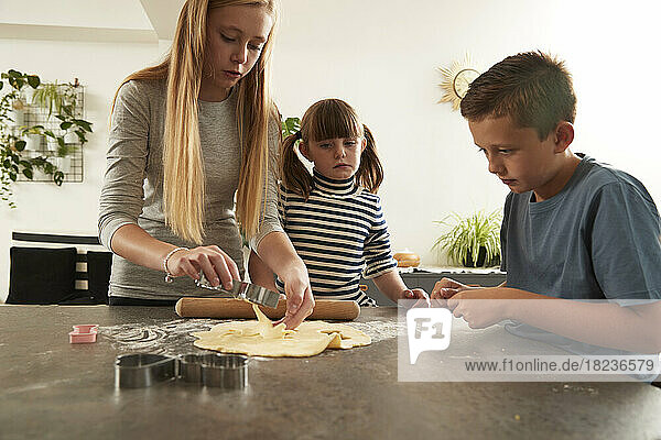 Boy looking at sister using cookie cutter standing by sister at home