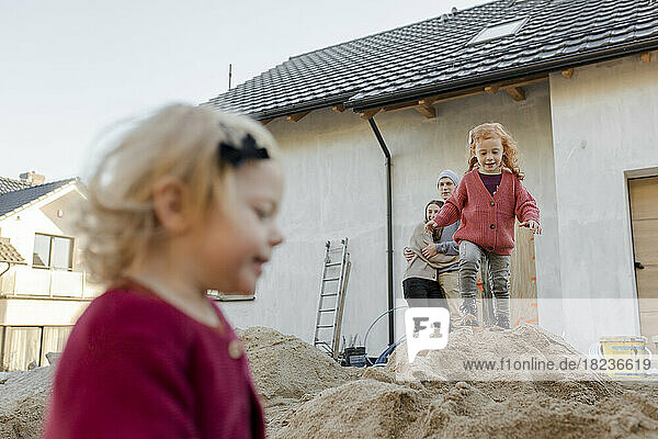 Girl playing on heap of cement with parents at construction site