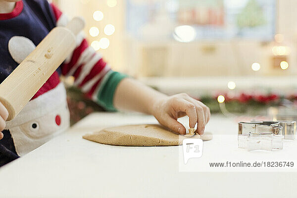 Hand of boy rolling gingerbread dough at kitchen counter