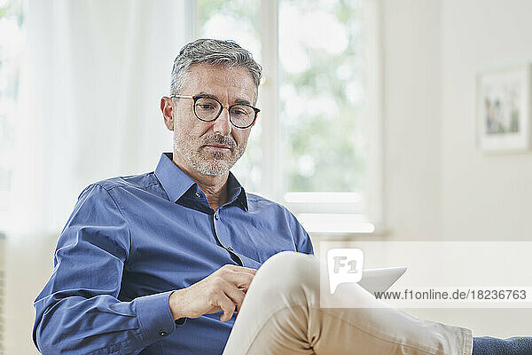 Mature businessman looking at tablet PC in armchair at home
