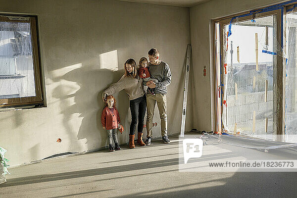 Geschwister mit Eltern stehen vor der Wand in einem unvollständigen Zuhause