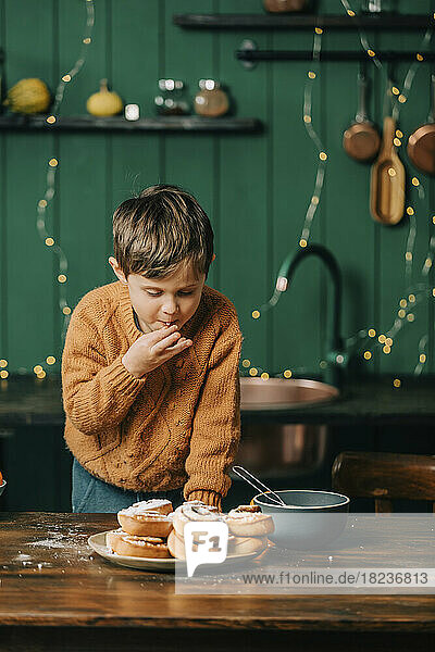 Boy eating cinnamon buns in kitchen at Christmas