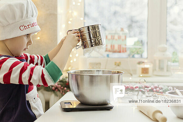 Boy sieving flour for gingerbread at kitchen counter