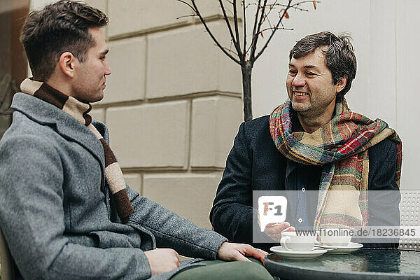 Glücklicher Vater und Sohn sitzen mit Kaffeetassen im Straßencafé