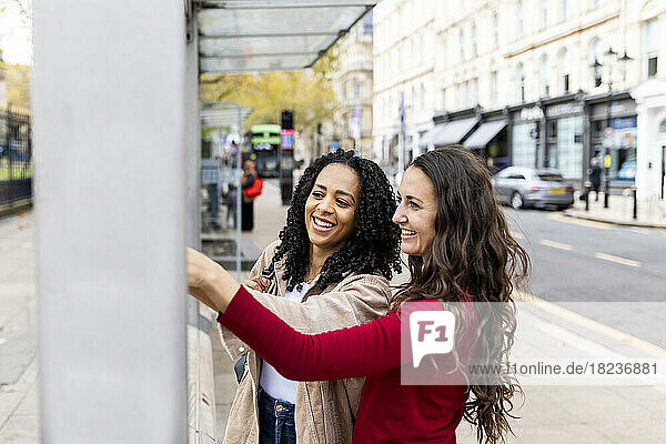 Fröhliche Freunde berühren die Wand auf dem Fußweg an der Bushaltestelle