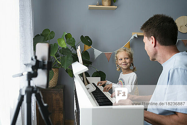 Smiling girl playing piano with father at home