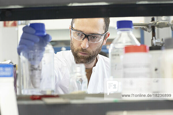 Scientist holding bottle seen through shelf in chemistry laboratory