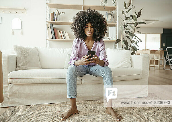 Junge Frau benutzt Mobiltelefon und sitzt auf dem Sofa im Wohnzimmer