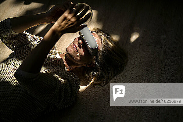 Mature woman wearing VR glasses and holding light bulb lying at home