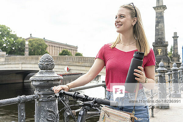 Happy young woman standing with bicycle at footpath