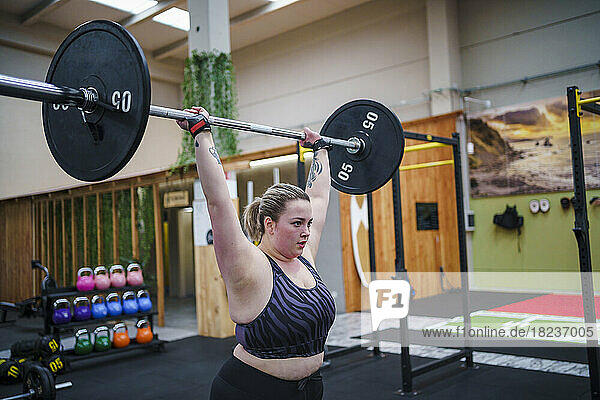Young woman with arms raised lifting barbell in gym