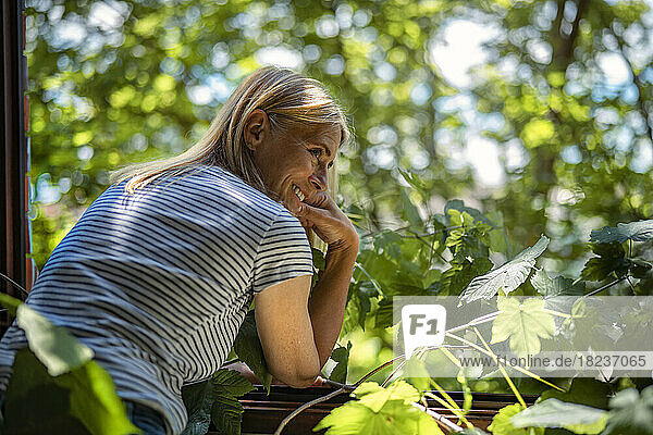 Smiling mature woman standing near window by plants at home