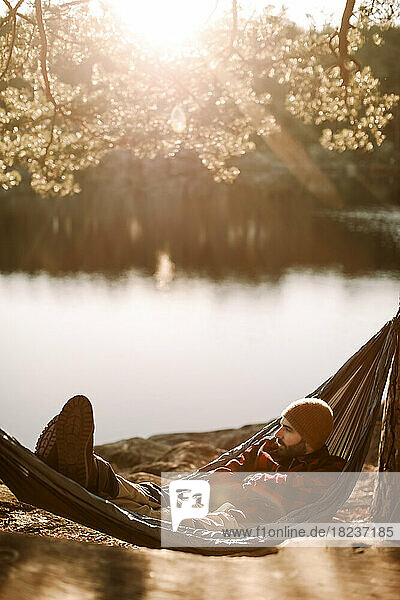 Mann entspannt sich auf Hängematte in der Nähe des Sees an einem sonnigen Tag