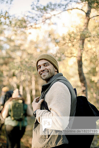 Side view of smiling man with backpack standing in forest