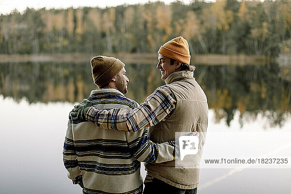 Männliche Freunde reden miteinander  während sie mit dem Arm gegen den See stehen
