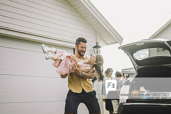 Glücklicher Vater spielt mit seiner Tochter im Elektroauto vor dem Haus