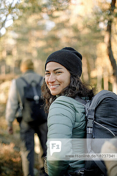 Happy woman looking over shoulder while hiking in forest