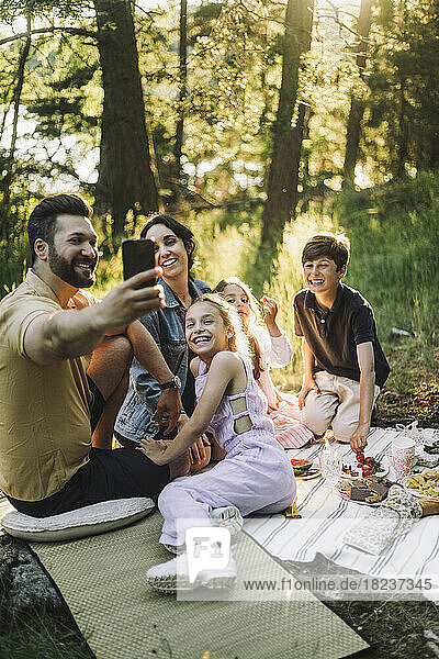 Vater macht beim Picknick ein Selfie mit seiner Familie über sein Smartphone
