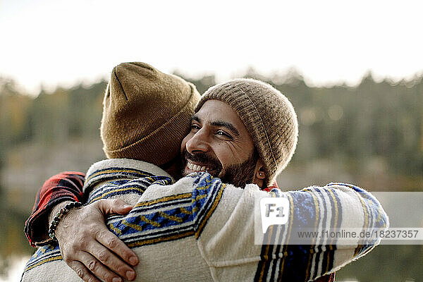 Happy male friends embracing each other wearing knit hats