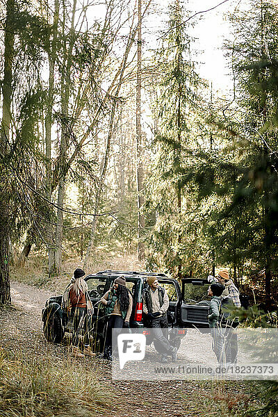 Männliche und weibliche Freunde verbringen ihre Freizeit in der Nähe eines Geländewagens im Wald