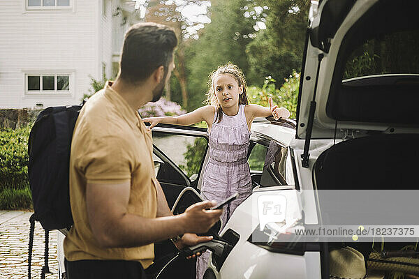 Tochter spricht mit Vater  der ein Elektroauto auflädt
