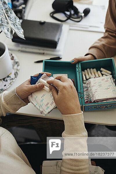 Hände einer Schülerin halten Binden und Tampons am Tisch im Schulbüro