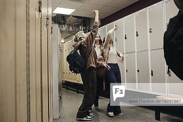 Full length of cheerful female students with hands raised enjoying in school corridor