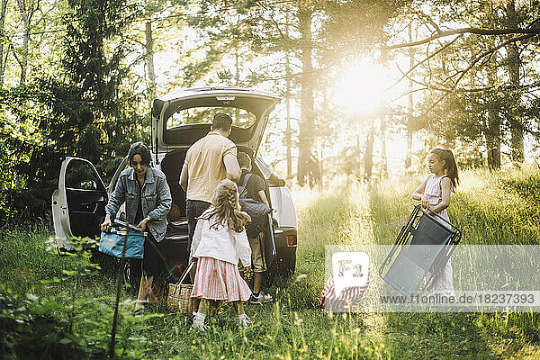 Eine Familie hilft sich gegenseitig beim Ausladen von Sachen aus dem Kofferraum eines Autos im Wald
