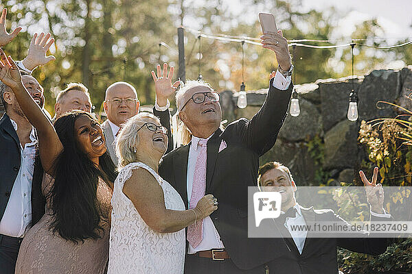 Glückliche frisch verheiratetes älteres Paar nimmt Selfie mit Familie und Freunden durch Smartphone