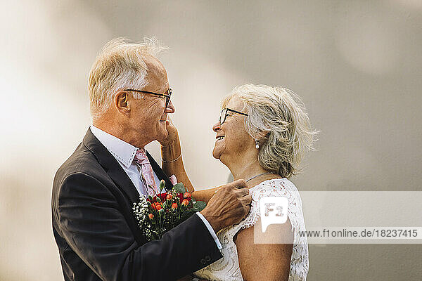 Seitenansicht eines lächelnden älteren Paares  das sich gegenseitig anschaut und an der Wand steht