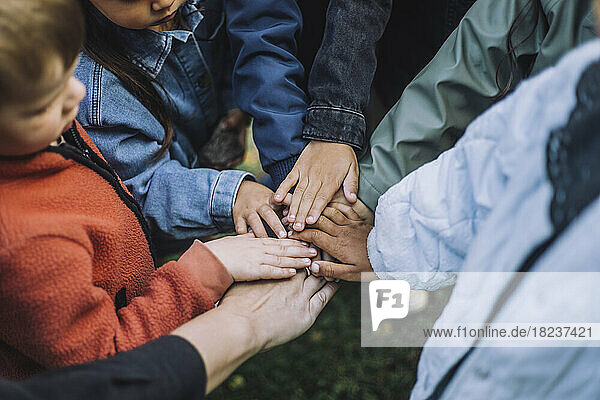 Verspielte multirassische Vorschüler stapeln Hände mit Lehrer im Park