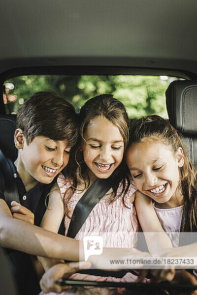 Glückliche Geschwister teilen sich einen Tablet-PC während einer Autofahrt