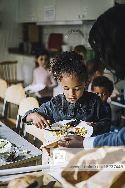Mädchen wirft Essensreste in eine Papiertüte  die von einer Lehrerin in der Kindertagesstätte gehalten wird