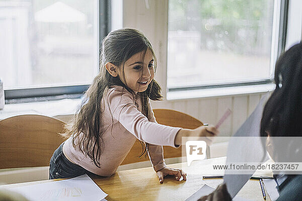 Lächelndes Mädchen  das auf den Lehrer zeigt  der eine Zeichnung während des Kunstunterrichts im Kindergarten zeigt