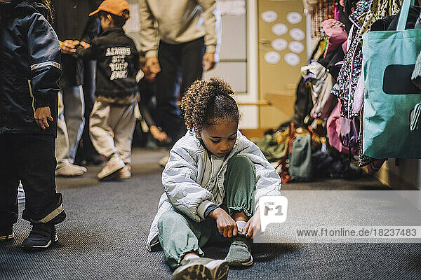 Mädchen trägt Schuh  während sie auf dem Teppich in der Kindertagesstätte sitzt