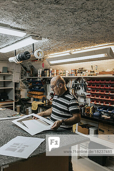 Senior craftsman with frame standing at workbench