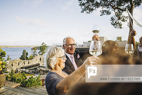Glückliche Freunde stoßen mit Weingläsern während einer Hochzeitsfeier an.