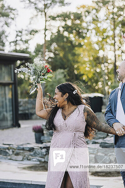 Fröhliche junge Braut mit Blumenstrauß und Bräutigam bei der Hochzeit