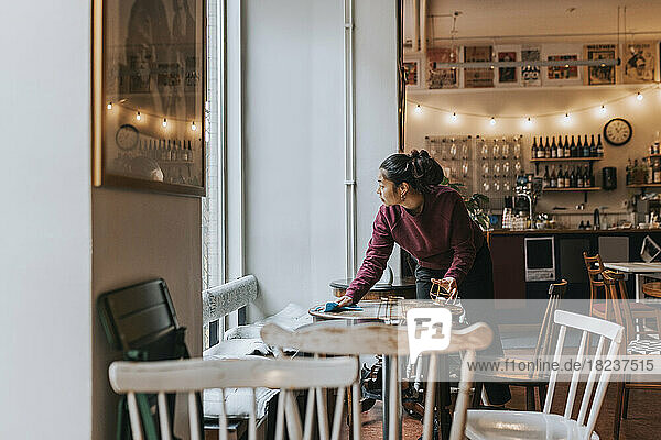 Unternehmerin reinigt Tisch mit Lappen bei der Arbeit im Café