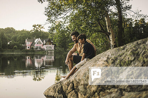 Vater und Sohn sitzen auf einem Felsen am See