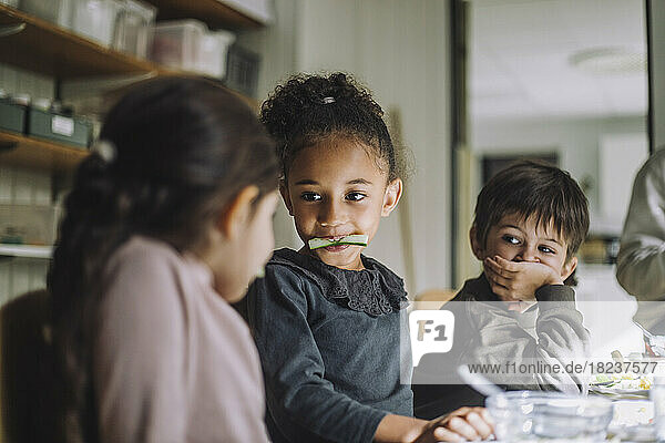 Multirassische Schülerinnen essen Gurke von männlichen Klassenkameraden in der Kindertagesstätte