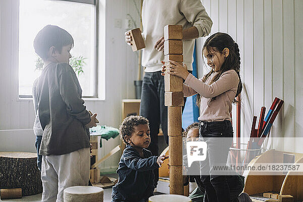 Weibliche und männliche Schüler stapeln Holzspielzeugklötze mit einem männlichen Lehrer in einer Kindertagesstätte