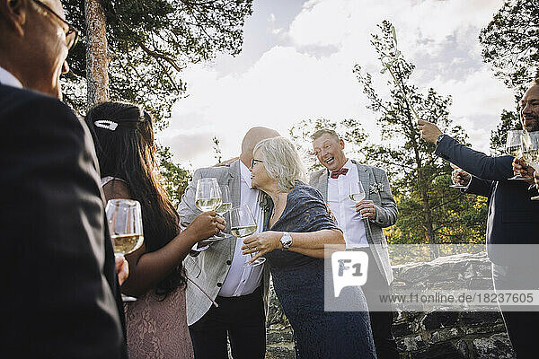 Ältere Frau umarmt Bräutigam mit Weingläsern inmitten der Hochzeitsgäste