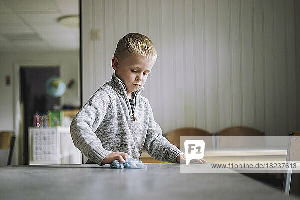 Junge reinigt Esstisch mit Serviette in Kindertagesstätte