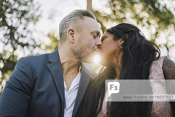 Back lit mature groom kissing young bride during wedding