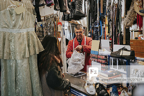 Rückansicht einer Kundin im Gespräch mit einem Ladenbesitzer  der eine Plastiktüte hält